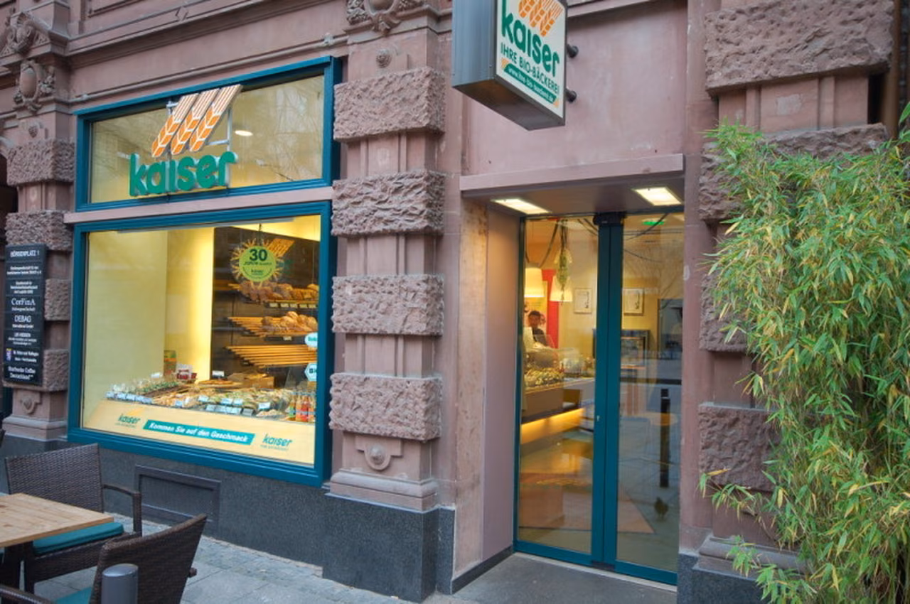 Bäckereifiliale mit grünem Schaufensterrahmen in einer Sandsteinfassade