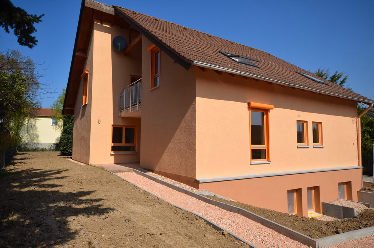 Umgebautes Wohnhaus mit orangefarbenen Fensterrahmen und Garten