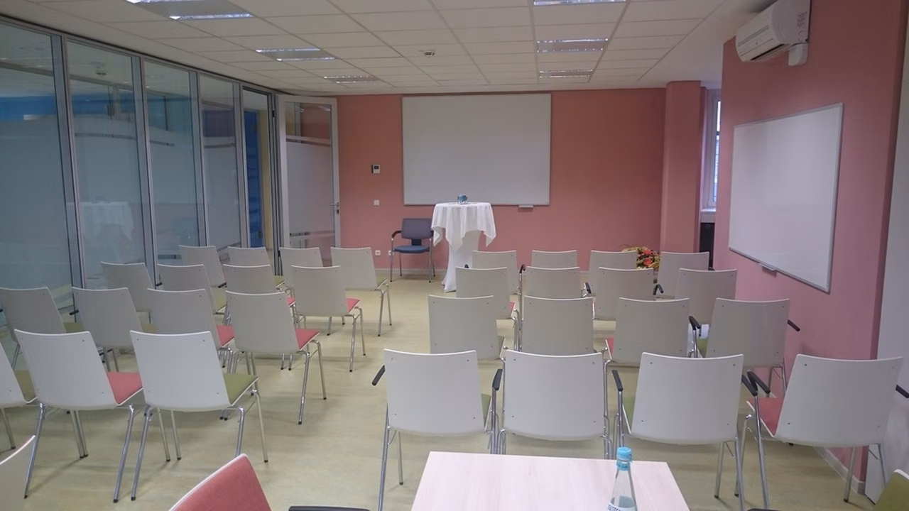 Gruppenraum mit Stuhlreihen vor einer rosa Wand