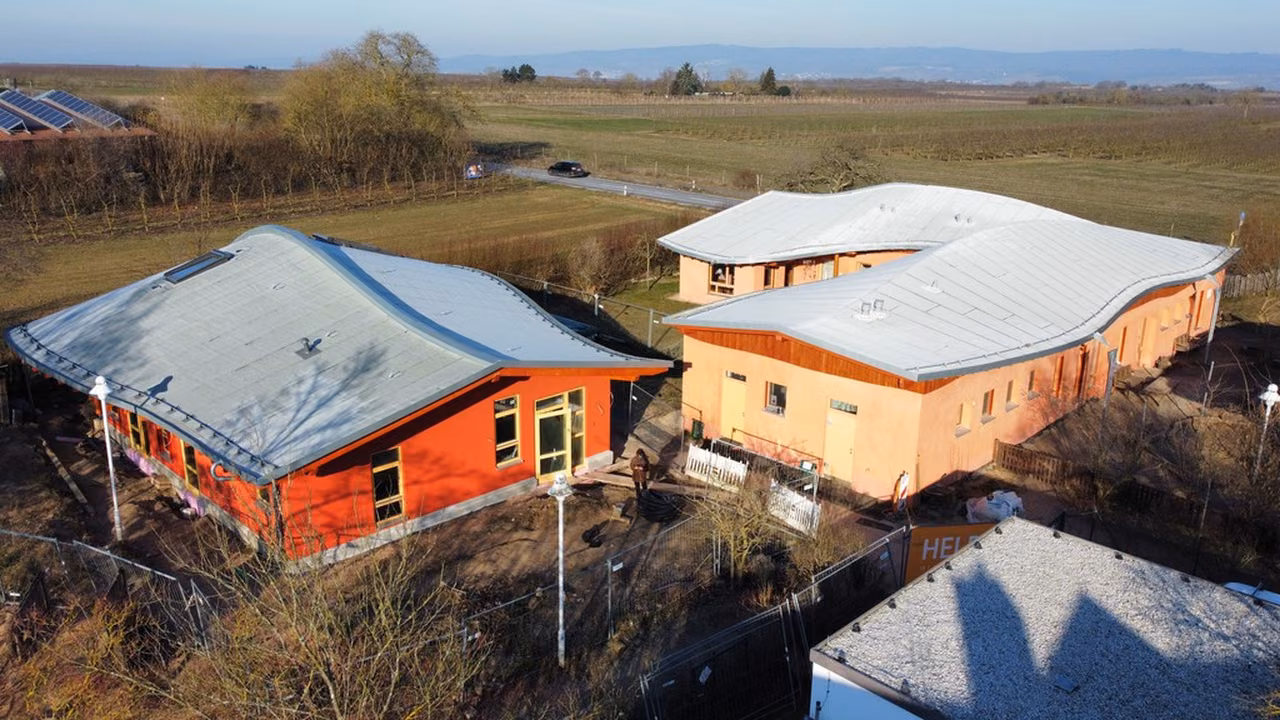 Kita-Neubau mit gewölbtem Dach und roter und ockerfarbener Fassade am Feldrand