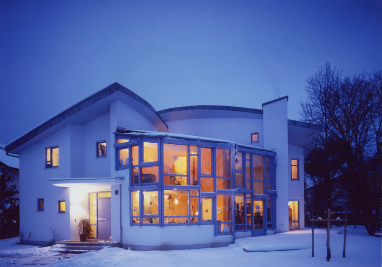 Wohnhaus mit beleuchtetem zweigeschossigem Wintergarten im Schnee